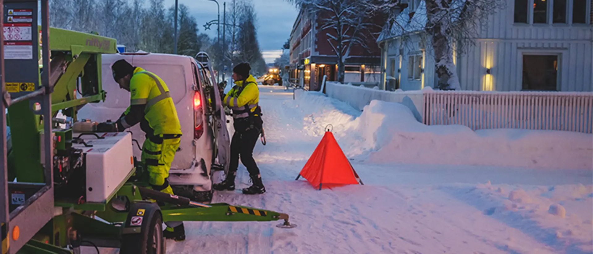 Två personer i varselkläder tar fram utrustning från en bil. Fotot är taget av Storgatan i Jokkmokk en vinterdag. foto: CJ Utsi