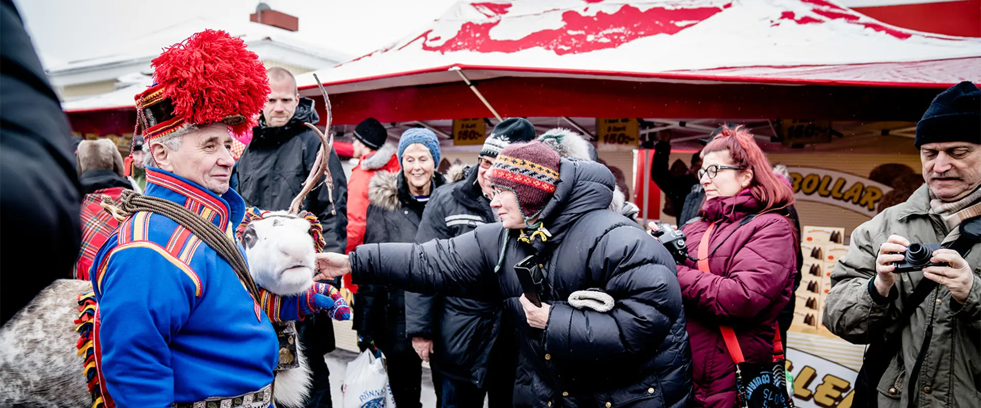 Marknadsvimmel vid Jokkmokks vintermarknad. Renrajden kommer gående med en ren. Foto.