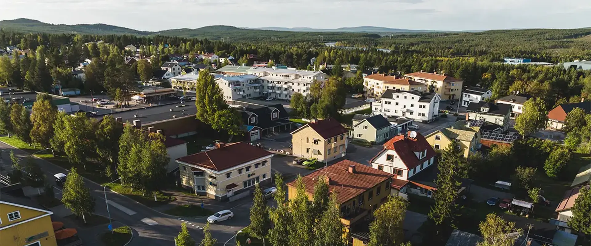 Översiktsbild över Jokkmokks tätort tagen under sommaren med hustak och trädtoppar i fokus. Foto: CJ Utsi