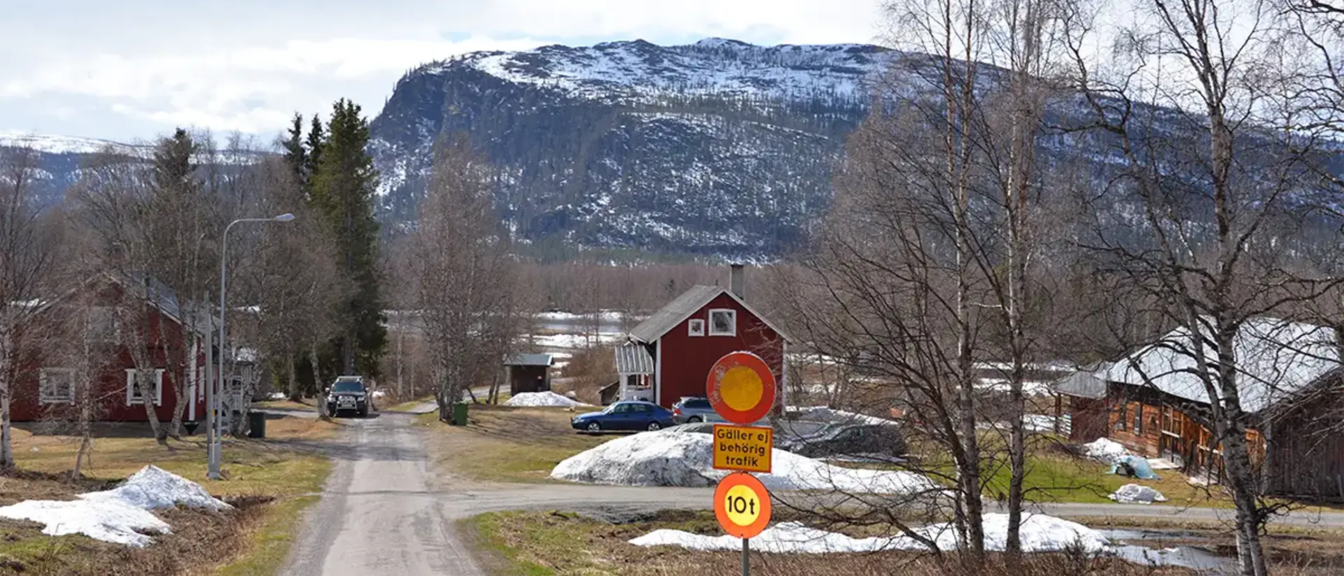 Liten väg ner mot båtlämning i Kvikkjokk. Två hus syns och en vägskylt. I bakgrunden syns berget Nammatj. Foto