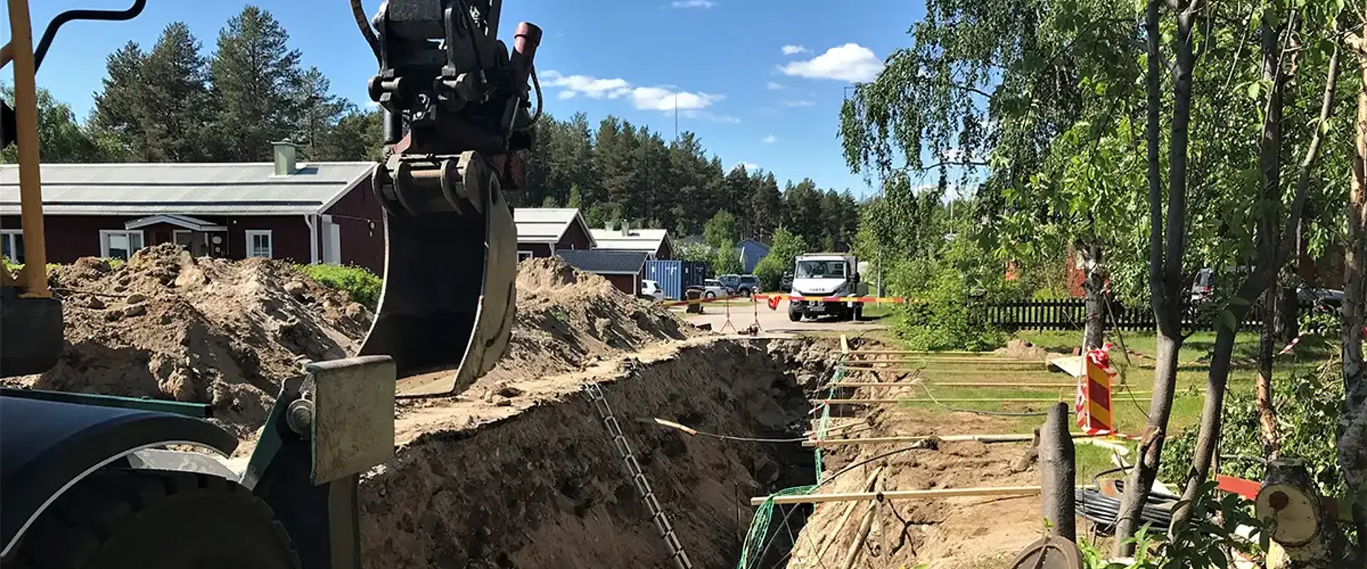 Grävarbete bredvid vägkant med fordon och dike där kablar syns. Sommar. Foto.